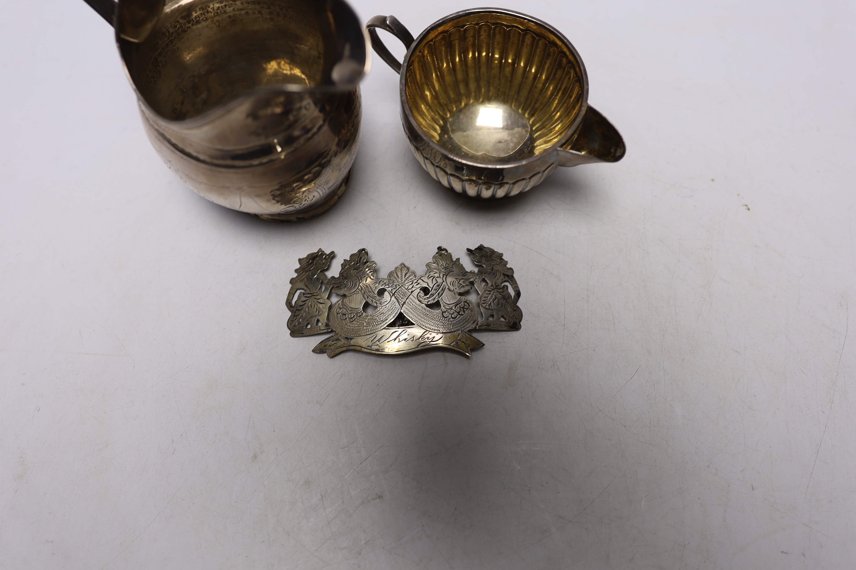 A George III silver helmet shaped cream jug, London, 1799 (a.f.), a Victorian silver cream jug by George Unite and a white metal whisky wine label.